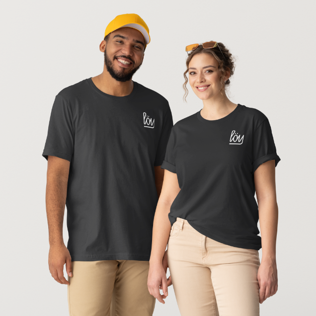 Two models wearing matching black crewneck t-shirts with a small white script logo on the left chest, standing against a light gray studio background.