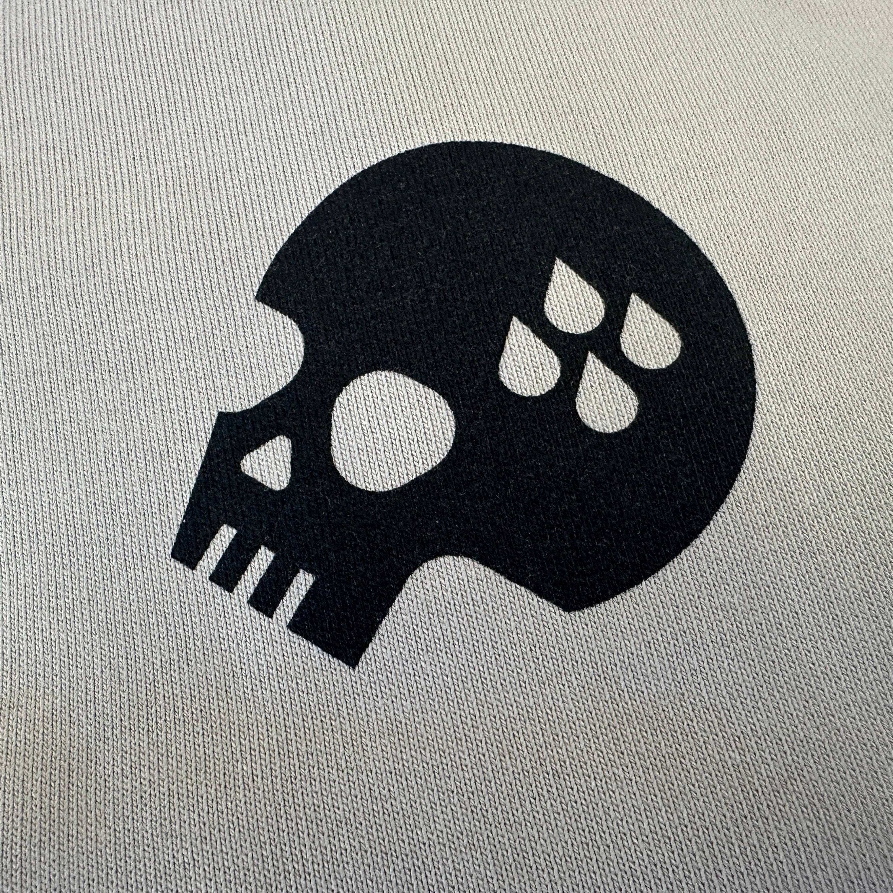A close-up of a black skull graphic printed on a light gray textured fabric background.